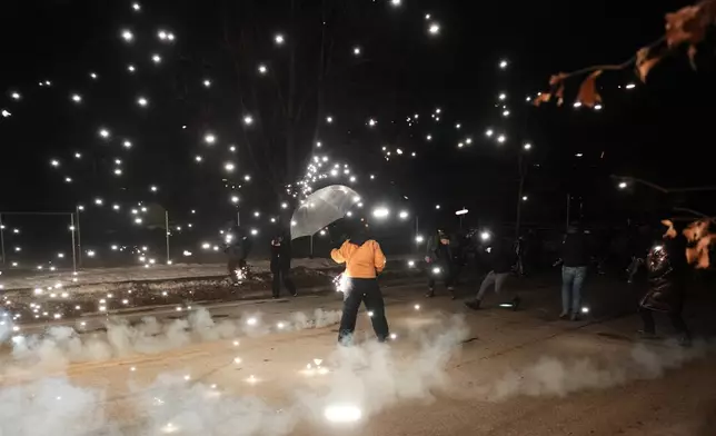 A protester holds an umbrella as sparks fly from a flash bang deployed by law enforcement on Wednesday, Jan. 14, 2026, in Minneapolis. (AP Photo/Adam Gray)