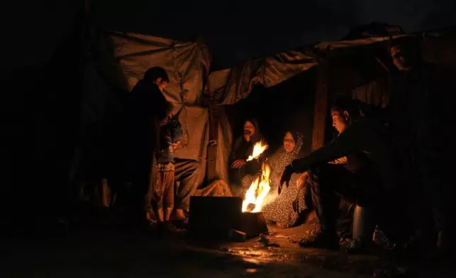 Displaced Palestinians warm themselves around a fire at a tent camp in Gaza City, Sunday, Jan. 18, 2026. (AP Photo/Jehad Alshrafi)