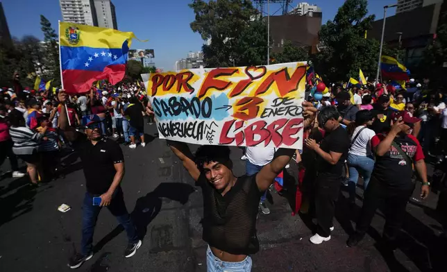 A Venezuelan celebrates holding a banner with a message that reads in Spanish: "At last Venezuela is free" after U.S. President Donald Trump announced that President Nicolas Maduro had been captured and flown out of Venezuela, in Santiago, Chile, Saturday, Jan. 3, 2026. (AP Photo/Esteban Felix)