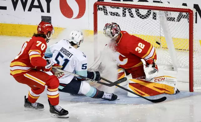 Seattle Kraken's Shane Wright, centre, scores on Calgary Flames goalie Dustin Wolf, right, as Ryan Lomberg defends during third period NHL hockey action in Calgary, Alberta, Monday, Jan. 5, 2026. (Jeff McIntosh/The Canadian Press via AP)