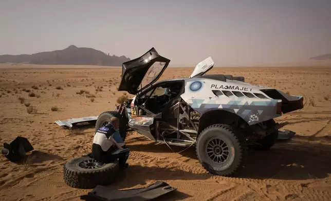 Driver Denis Krotov sits on a tire as co-driver Konstantin Zhiltsov, unseen, repairs their car after they stopped for a bivouac at the end of the fourth stage of the Dakar Rally between Alula and Hail, Saudi Arabia, Wednesday, Jan. 7, 2026. (AP Photo/Thibault Camus)