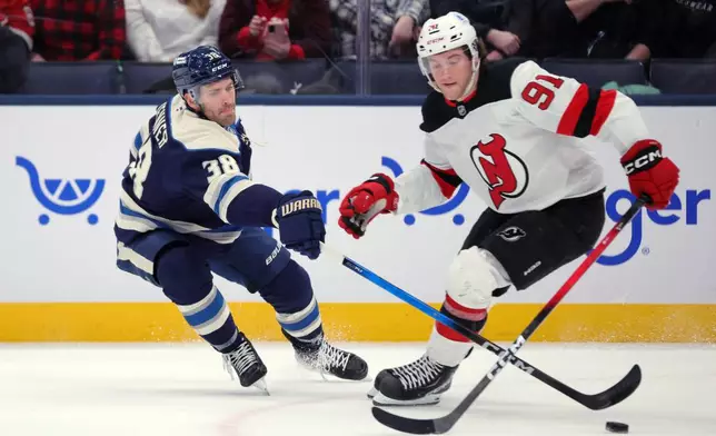 Columbus Blue Jackets forward Boone Jenner, left, knocks the puck away from New Jersey Devils forward Dawson Mercer during the first period of an NHL hockey game in Columbus, Ohio, Wednesday, Dec. 31, 2025. (AP Photo/Paul Vernon)