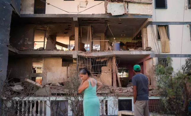 Residents look at a damaged apartment complex that neighbors say was hit during U.S. strikes to capture Venezuelan President Nicolás Maduro, in Catia La Mar, Venezuela, Sunday, Jan. 4, 2026. (AP Photo/Matias Delacroix)