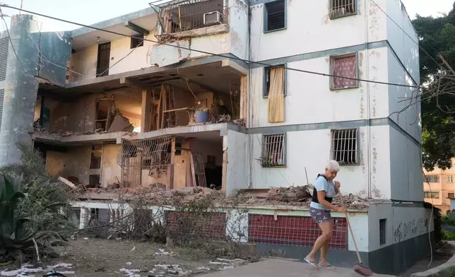 Carmen Mejias sweeps in front of a damaged apartment complex that neighbors say was hit during U.S. strikes to capture Venezuelan President Nicolás Maduro, in Catia La Mar, Venezuela, Sunday, Jan. 4, 2026. (AP Photo/Matias Delacroix)