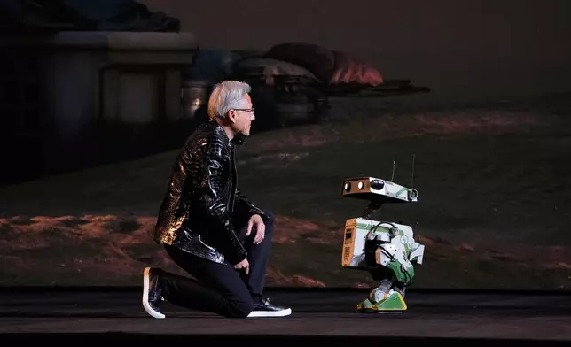 Nvidia founder and CEO Jensen Huang kneels in front of a robot during a Nvidia news conference ahead of the CES tech show Monday, Jan. 5, 2026, in Las Vegas. (AP Photo/John Locher)