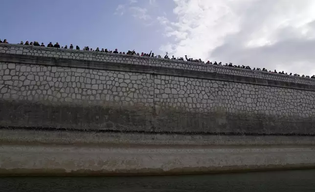 People attend the Epiphany ceremony as a Greek Orthodox priest, center, holding a cross blesses the waters at Lake Marathon, near Athens, on Tuesday, Jan. 6, 2026, where receding water levels reflect successive years of low rainfall across Greece. (AP Photo/Thanassis Stavrakis)