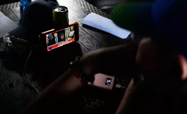 Government supporters watch on a smartphone a press conference by U.S. President Donald Trump explaining details of the operation in which U.S. forces captured and removed President Nicolás Maduro, in Caracas, Venezuela, Saturday, Jan. 3, 2026. (AP Photo/Ariana Cubillos)