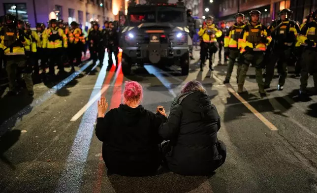 Two people sit in the street holding hands in front of Minnesota State Patrol during a protest and noise demonstration calling for an end to federal immigration enforcement operations in the city, Friday, Jan. 9, 2026, in Minneapolis. (AP Photo/John Locher)