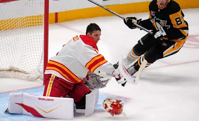 Calgary Flames goaltender Devin Cooley has his mask knocked off by a shot on goal with Pittsburgh Penguins' Ben Kindel (81) unable to get to the rebound during the first period of an NHL hockey game in Pittsburgh, Saturday, Jan. 10, 2026. (AP Photo/Gene J. Puskar)