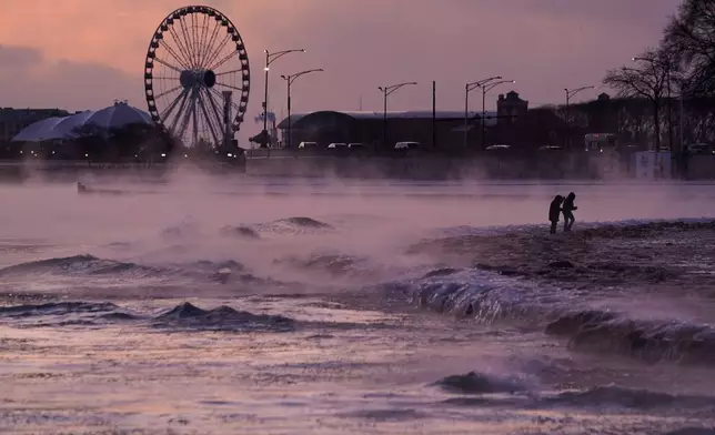 People walk on an ice covered beach along the shore of Lake Michigan, Friday, Jan. 23, 2026, in Chicago. (AP Photo/Kiichiro Sato)
