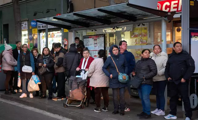 People from several Latin American countries, including Colombia, Peru and the Dominican Republic, along with Spaniards, wait at a bus stop in L'Hospitalet de Llobregat, near Barcelona, Spain, Friday, Jan. 30, 2026. (AP Photo/Emilio Morenatti)