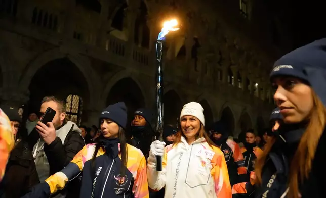 A torchbearer holds an Olympic torch flame in Venice, Italy, Thursday, Jan. 22, 2026, and its journey will conclude in Milan on February 6 for the Winter Olympics opening ceremony. (AP Photo/Luca Bruno)