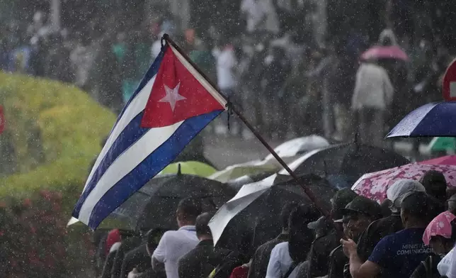 People line up outside the Ministry of the Revolutionary Armed Forces where the remains are on display of the Cuban officers who were killed during the U.S. operation in Venezuela that captured President Nicolas Maduro, as it sprinkles rain in Havana, Cuba, Thursday, Jan. 15, 2026. (AP Photo/Ramon Espinosa)