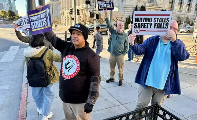Demonstrators holds signs during a protest by Uber and Lyft drivers asking state regulators to take self-driving taxis off the streets due to safety concerns at the California Public Utilities Commission headquarters Friday, Jan. 9, 2026, in San Francisco. (AP Photo/Haven Daley)