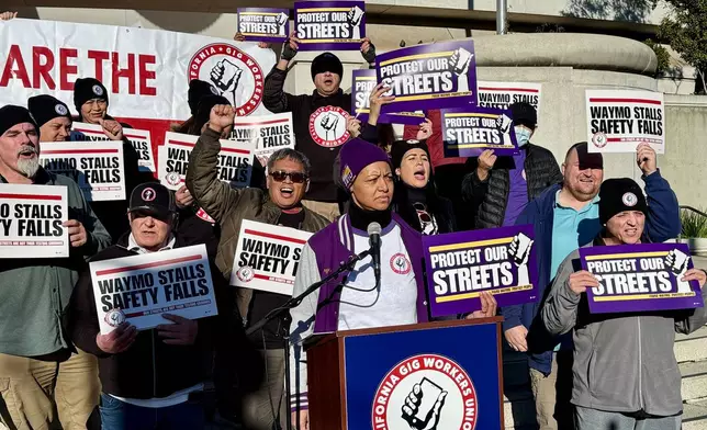 Demonstrators holds signs during a protest by Uber and Lyft drivers asking state regulators to take self-driving taxis off the streets due to safety concerns at the California Public Utilities Commission headquarters Friday, Jan. 9, 2026, in San Francisco. (AP Photo/Haven Daley)