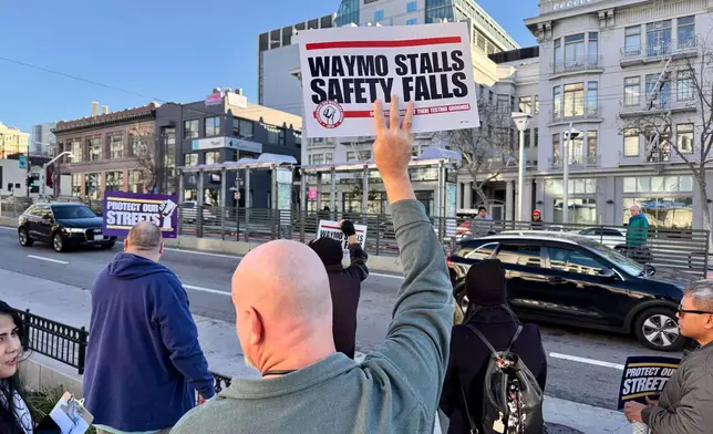 Demonstrators holds signs during a protest by Uber and Lyft drivers asking state regulators to take self-driving taxis off the streets due to safety concerns at the California Public Utilities Commission headquarters Friday, Jan. 9, 2026, in San Francisco. (AP Photo/Haven Daley)