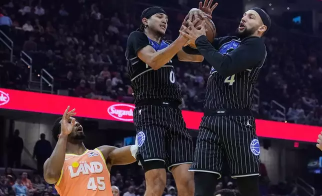 Orlando Magic guard Anthony Black (0) and guard Jalen Suggs (4) grab a rebound in front of Cleveland Cavaliers guard Donovan Mitchell (45) in the first half of an NBA basketball game in Cleveland, Monday, Jan. 26, 2026. (AP Photo/Sue Ogrocki)