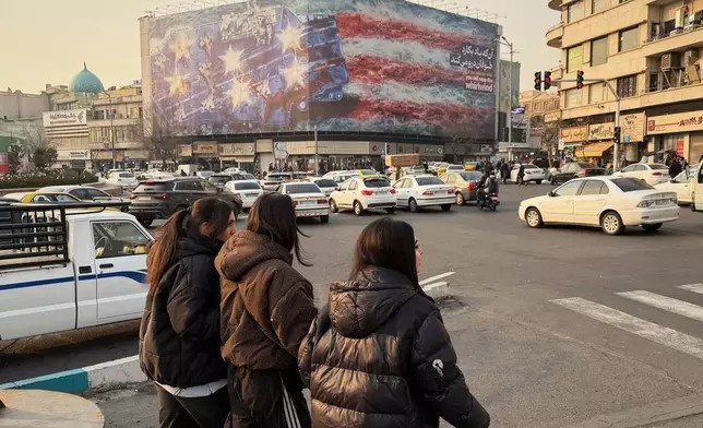 People walk in front a billboard with graphic showing a U.S aircraft carrier with damaged fighter jets on its deck, and sign reading in Farsi and English: "If you sow the wind, you'll reap whirlwind," at the Enqelab-e-Eslami (Islamic Revolution) square, in Tehran, Iran, Sunday, Jan. 25, 2026. (AP Photo/Vahid Salemi)