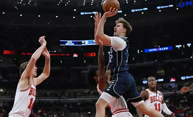 Dallas Mavericks' Cooper Flagg goes up for a shot against Chicago Bulls' Coby White and Matas Buzelis (14) during the first half of an NBA basketball game, Saturday, Jan. 10, 2026, in Chicago. (AP Photo/Paul Beaty)
