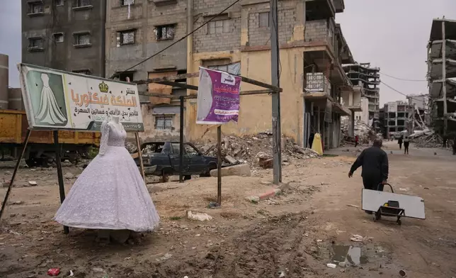 A Palestinian man walks past a wedding dress displayed on a street next to a bridal shop in Khan Younis, southern Gaza Strip, Thursday, Jan. 22, 2026. (AP Photo/Abdel Kareem Hana)