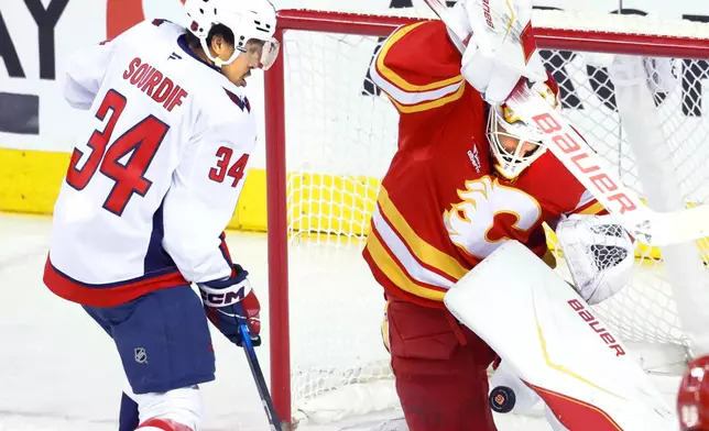 Washington Capitals' Justin Sourdif (34) looks for a rebound as Calgary Flames goalie Devin Cooley makes a save during the third period of an NHL hockey game in Calgary, Alberta, Friday, Jan. 23, 2026. (Larry MacDougal/The Canadian Press via AP)