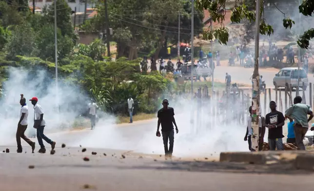 FILE - A man holds a rock as riot police fire tear gas at a crowd of angry voters outside a polling station where voting material for the presidential election never arrived, at a polling station in Ggaba, on the outskirts of Kampala, in Uganda Thursday, Feb. 18, 2016. (AP Photo/Ben Curtis, File)