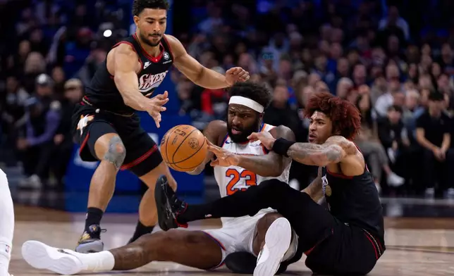 New York Knicks' Mitchell Robinson, center, tries to pass the ball with Philadelphia 76ers' Kelly Oubre Jr., right, and Quentin Grimes, left, defending during the first half of an NBA basketball game, Saturday, Jan. 24, 2026, in Philadelphia. (AP Photo/Chris Szagola)
