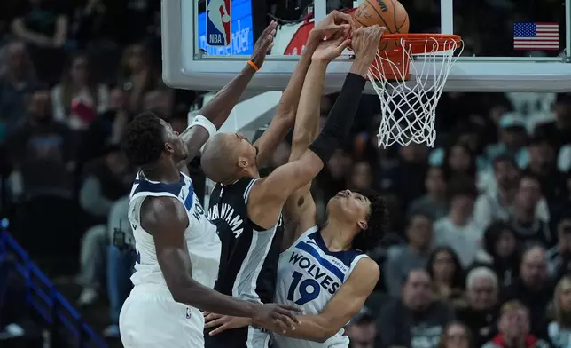 San Antonio Spurs forward Victor Wembanyama, center, scores against Minnesota Timberwolves guard Anthony Edwards, left, and forward Joan Beringer (19) during the second half of an NBA basketball game in San Antonio, Saturday, Jan. 17, 2026. (AP Photo/Eric Gay)