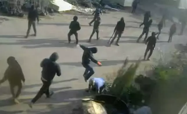 This frame grab from security camera footage filmed Jan. 8, 2026, and obtained by The Associated Press, shows men dressed mostly in black with their faces covered, one of whom is kicking a man on the ground as he tried to flee a nursery in the northern West Bank village of Deir Sharaf. Two people who witnessed the attack and are members of the family that owns the facility said the assailants were Israeli settlers beating 67-year-old Basim Saleh Yassin.(UGC via AP)