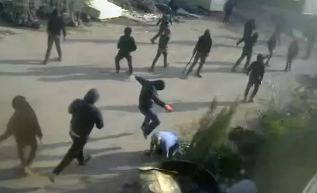 This frame grab from security camera footage filmed Jan. 8, 2025, and obtained by The Associated Press, shows men dressed mostly in black with their faces covered, one of whom is kicking a man on the ground as he tried to flee a nursery in the northern West Bank village of Deir Sharaf. Two people who witnessed the attack and are members of the family that owns the facility said the assailants were Israeli settlers beating 67-year-old Basim Saleh Yassin.(UGC via AP)