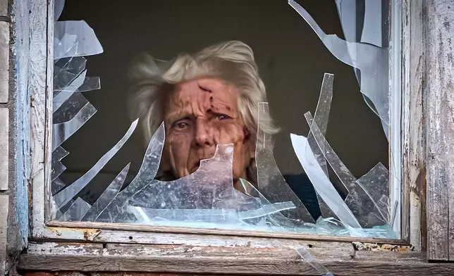 FILE - An injured elderly woman looks out of her broken window as an apartment building was hit by a Russian drone during an aerial attack in Kyiv, Ukraine, Dec. 23, 2025. (AP Photo/Efrem Lukatsky, File)
