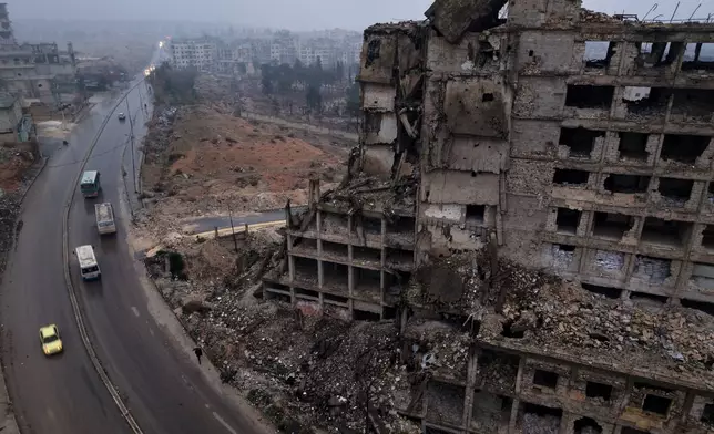 Buses carrying displaced residents drive past a building in ruins as they return to the Achrafieh neighborhood after days of fighting between government forces and Kurdish fighters in the northern city of Aleppo, Syria, Monday, Jan. 12, 2026. (AP Photo/Omar Albam)