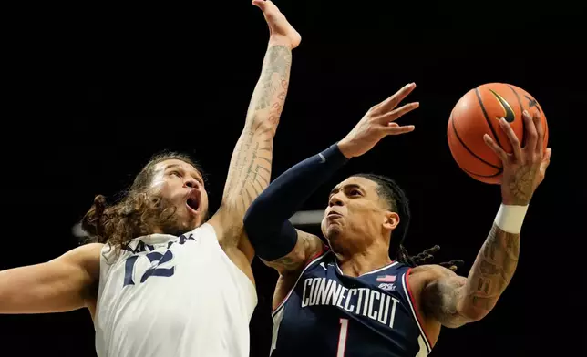 UConn guard Solo Ball (1) drives to the basket as Xavier forward Tre Carroll (12) defends during the second half of an NCAA college basketball game, Wednesday, Dec. 31, 2025, in Cincinnati. (AP Photo/Carolyn Kaster)