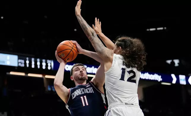 UConn forward Alex Karaban (11) shoots the ball as Xavier forward Tre Carroll (12) defends during the second half of an NCAA college basketball game, Wednesday, Dec. 31, 2025, in Cincinnati. (AP Photo/Carolyn Kaster)
