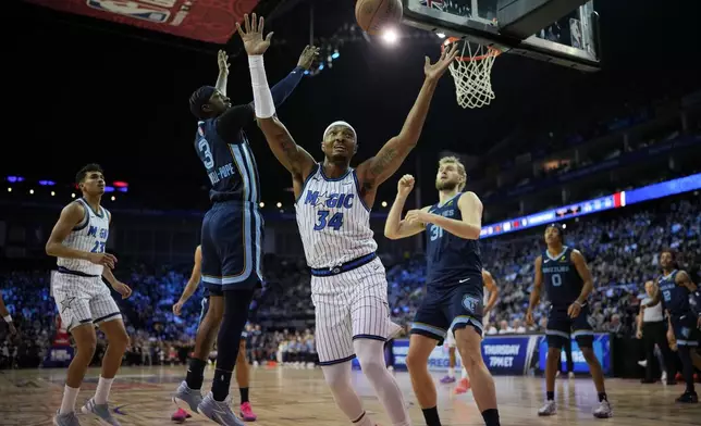 Orlando Magic center Wendell Carter Jr. (34) reaches for the ball as Memphis Grizzlies guard Kentavious Caldwell-Pope (3) and Memphis Grizzlies center Jock Landale (31) look on during the first half of NBA basketball game Sunday, Jan. 18, 2026, in London. (AP Photo/Kin Cheung)
