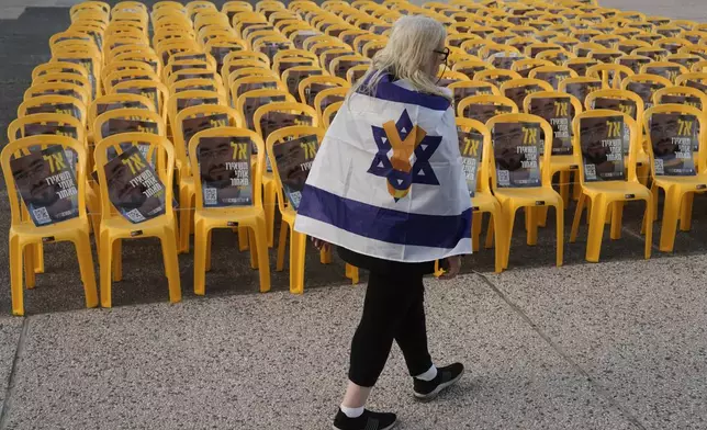 A woman walks by chairs with photo of Ran Gvili, the final hostage in Gaza who was killed while fighting Hamas militants during the Oct. 7, 2023 attack and whose remains have been recovered Monday, clearing the way for the next phase of the ceasefire that paused the Israel-Hamas war, in a plaza known as Hostages Square in Tel Aviv, Israel, Monday, Jan. 26, 2026. (AP Photo/Oded Balilty)