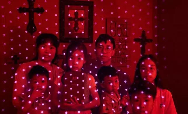 FILE - Members of a Chinese church living in exile after fleeing from China, are illuminated by beams of pulsed laser light from a cellphone's LiDAR scanner as they sit for a photo, Oct. 12, 2025, in Midland, Texas. Photographed are Wensheng Wen, rear right, his wife, Lou Guangyzing, and their children Xin, 11, from right, Gehua, 9, Jinghua, 3, Rou, 6, and Younghua, 3. (AP Photo/David Goldman, File)