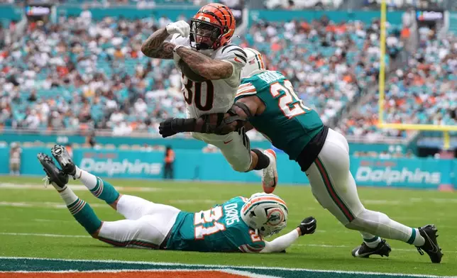 FILE - Cincinnati Bengals running back Chase Brown, center, breaks a tackle by Miami Dolphins linebacker Jordyn Brooks, right, for a touchdown during the second half of an NFL football game, Dec. 21, 2025, in Miami Gardens, Florida. (AP Photo/Lynne Sladky, File)