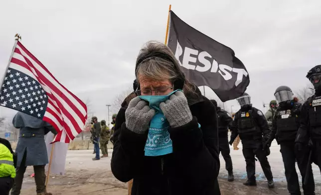 A woman covers her face from tear gas as federal immigration officers confront protesters outside Bishop Henry Whipple Federal Building, Thursday, Jan. 15, 2026, in Minneapolis. (AP Photo/Adam Gray)