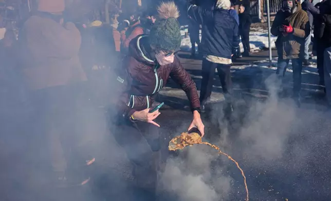 A protester pours liquid on a tear gas canister deployed by federal immigration officers near the scene where Renee Good was fatally shot by an ICE officer last week, Tuesday, Jan. 13, 2026, in Minneapolis. (AP Photo/John Locher)