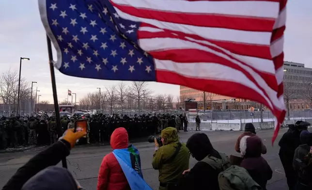 A person holds an upside-down American flag as law enforcement stand during a protest outside the Bishop Henry Whipple Federal Building on Saturday, Jan. 17, 2026, in Minneapolis. (AP Photo/Yuki Iwamura)
