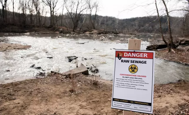 A recently placed warning sign is seen at the sight of a massive pipe rupture, as sewage flows into the Potomac River, right, in Glen Echo, Md., Friday, Jan. 23, 2026. A massive pipe that moves millions of gallons of sewage has ruptured and sent wastewater flowing into the Potomac River northwest of Washington, polluting it ahead of a major winter storm that has repair crews scrambling. (AP Photo/Cliff Owen)