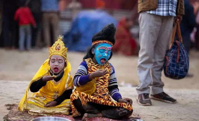 Children dressed as Hindu God Shiva, right, and Parvati eat on the side of street on the eve of Mauni Amavasya, a divine occasion in Hindu religious practice followed for honoring ancestors or forefathers, at the Sangam, the confluence of the Ganges, the Yamuna and the mythical Saraswati rivers, during the annual month long Hindu religious fair "Magh Mela" in Prayagraj, India, Saturday, Jan. 17, 2026. (AP Photo/Rajesh Kumar Singh)