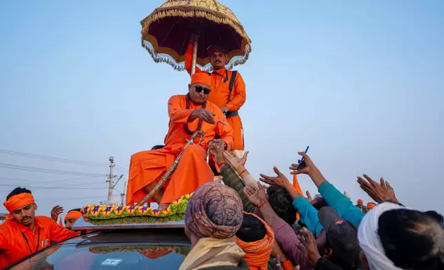 A Hindu holy man distributes food while sitting on the top of his vehicle on the eve of Mauni Amavasya, a divine occasion in Hindu religious practice followed for honoring ancestors or forefathers, at the Sangam, the confluence of the Ganges, the Yamuna and the mythical Saraswati rivers, during the annual month long Hindu religious fair "Magh Mela" in Prayagraj, India, Saturday, Jan.17, 2026. (AP Photo/Rajesh Kumar Singh)