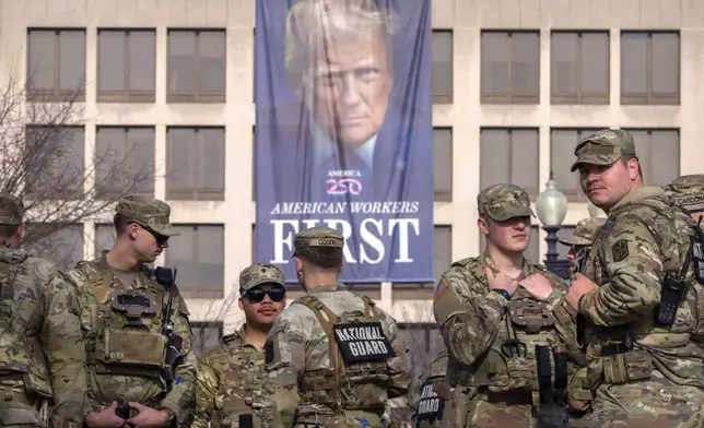 National Guard members gather near a large portrait of President Donald Trump on the Labor Department headquarters before the body of Metropolitan Police Department officer Terry Bennett is driven past the Capitol, Thursday, Jan. 8, 2026, in Washington. (AP Photo/Mark Schiefelbein)