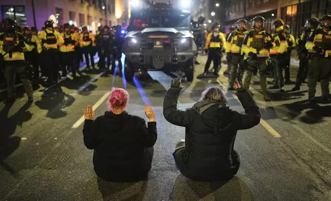 Two people sit in the street with their hands up in front of Minnesota State Patrol during a protest and noise demonstration calling for an end to federal immigration enforcement operations in the city, Friday, Jan. 9, 2026, in Minneapolis. (AP Photo/John Locher)