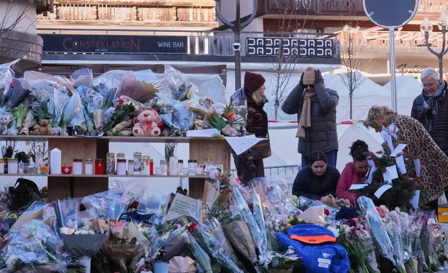 People lay flowers at the sealed off Le Constellation bar in Crans-Montana, Swiss Alps, Switzerland, Saturday, Jan. 3, 2026, where a devastating fire left dead and injured during the New Year's celebrations. (AP Photo/Antonio Calanni)