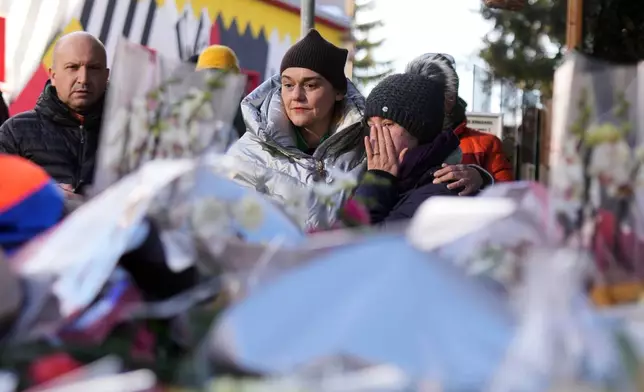 People mourn behind flowers and letters near the sealed off Le Constellation bar, where a devastating fire left dead and injured during the New Year's celebrations in Crans-Montana, Swiss Alps, Switzerland, Friday, Jan. 2, 2026. (AP Photo/ Antonio Calanni)