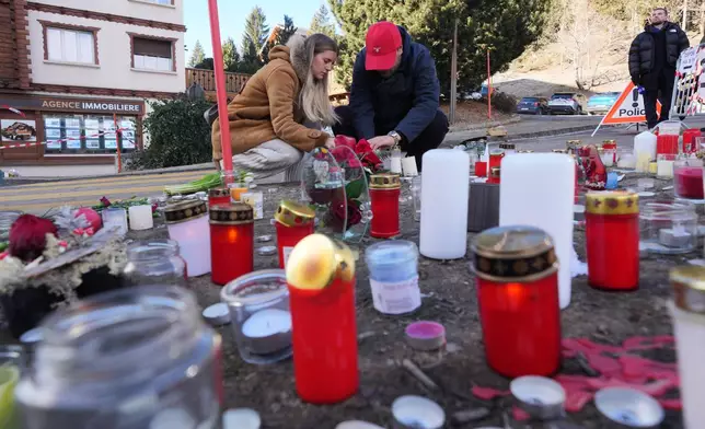 People bring flowers and candles near the sealed off Le Constellation bar, where a devastating fire left dead and injured during the New Year's celebrations in Crans-Montana, Swiss Alps, Switzerland, Friday, Jan. 2, 2026. (AP Photo/ Antonio Calanni)