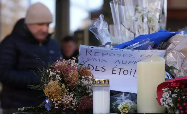 People bring flowers and letters, reading "Rest in Peace", near the sealed off Le Constellation bar, where a devastating fire left dead and injured during the New Year's celebrations in Crans-Montana, Swiss Alps, Switzerland, Friday, Jan. 2, 2026. (AP Photo/ Antonio Calanni)